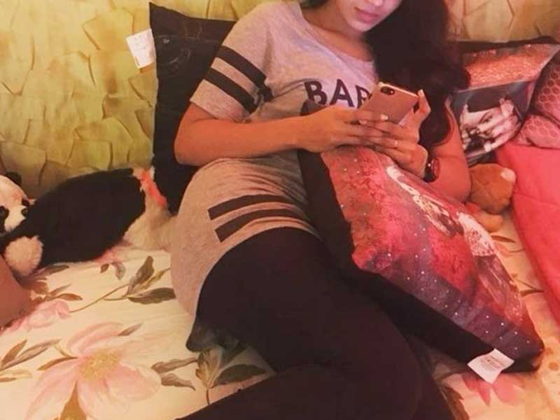 a girl in grey t-shirt and lower, lying in bed and using her phone